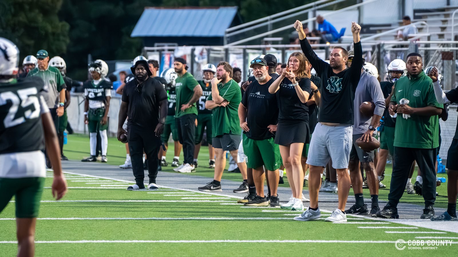 Coach Jarvis stands next to the JV defensive coaches sending in signals