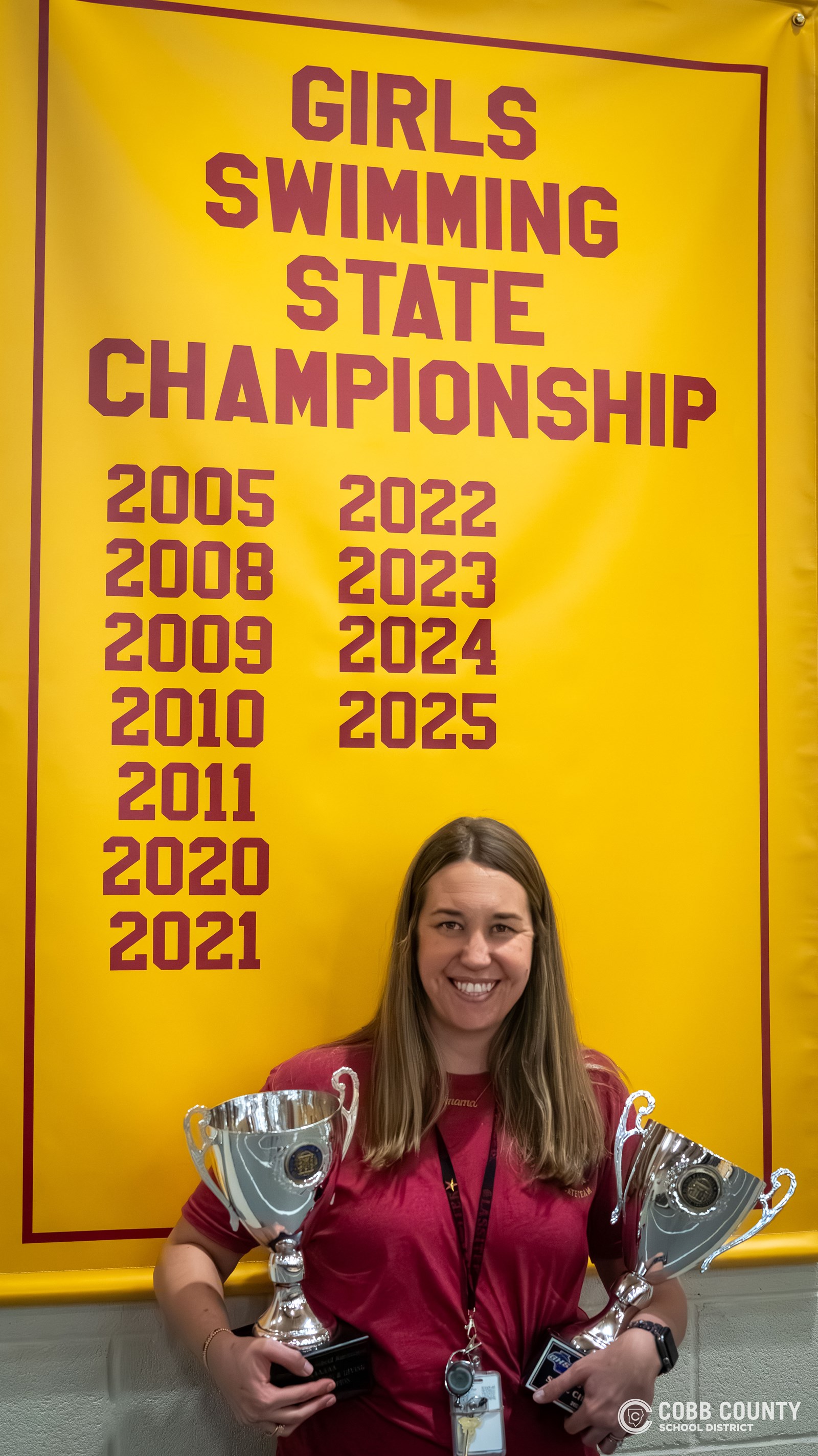 Coach Hughes poses with the Girls Swimming State Championship banner
