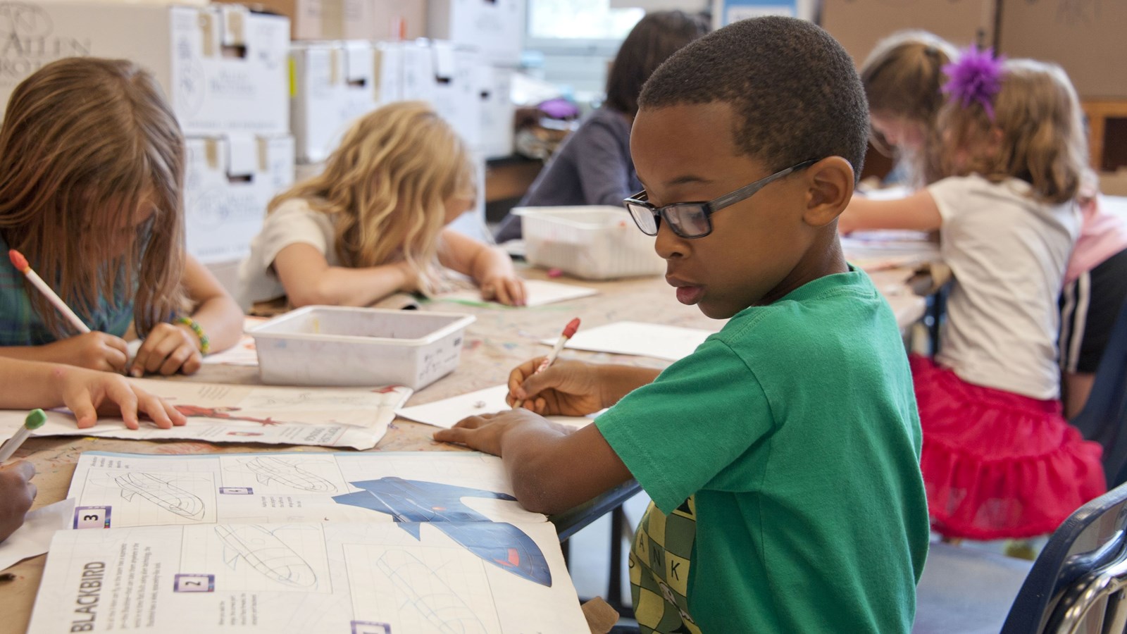 children sitting at a table with paper and pencils