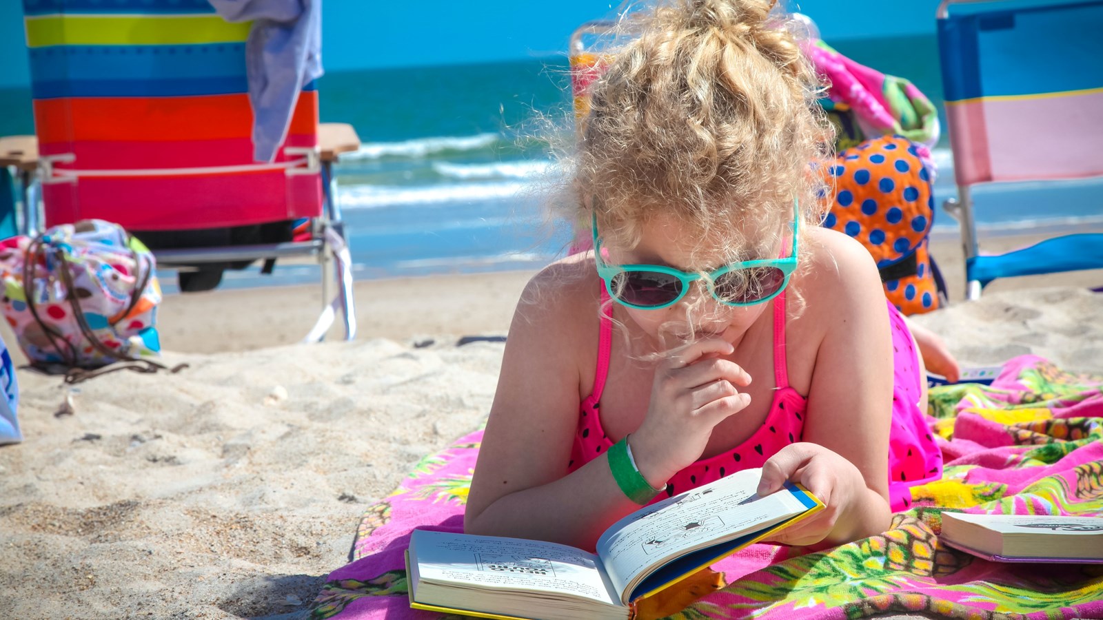 Child on the beach reading a book. 
