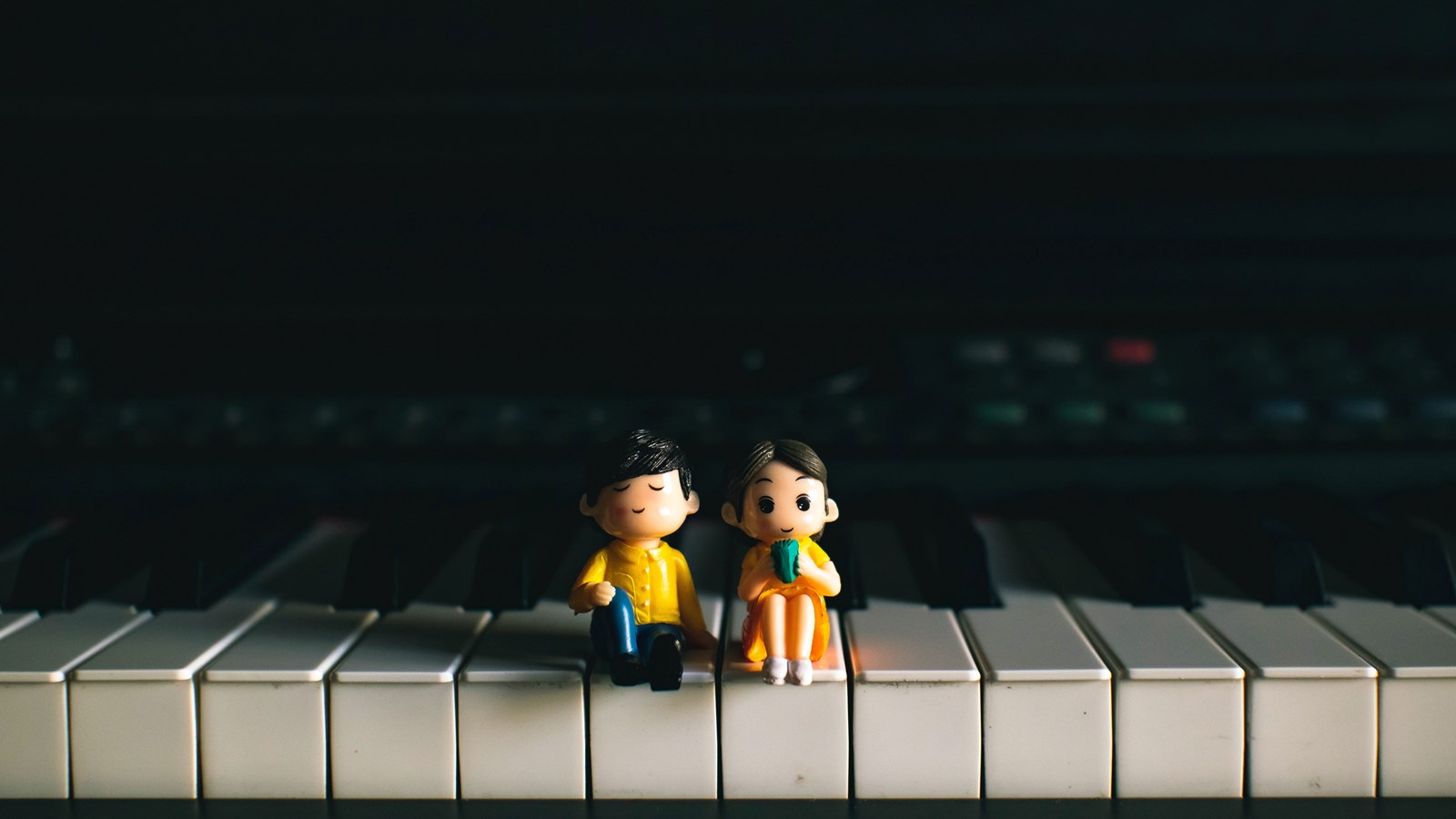 two tiny dolls sitting on a piano keyboard